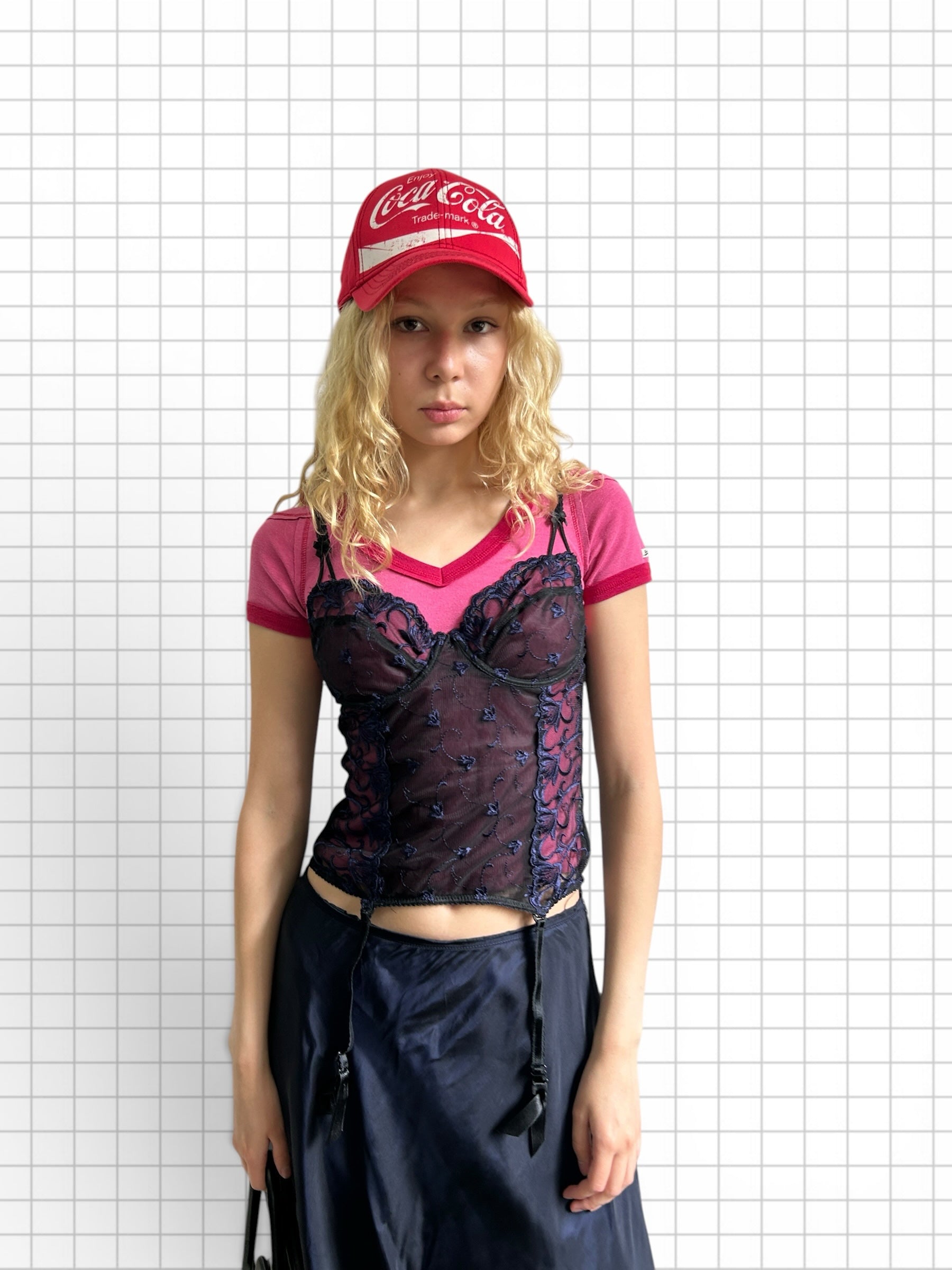 Wieder Wieder embroidered dark blue lace corset top with attached garters worn over a pink t-shirt and red cap