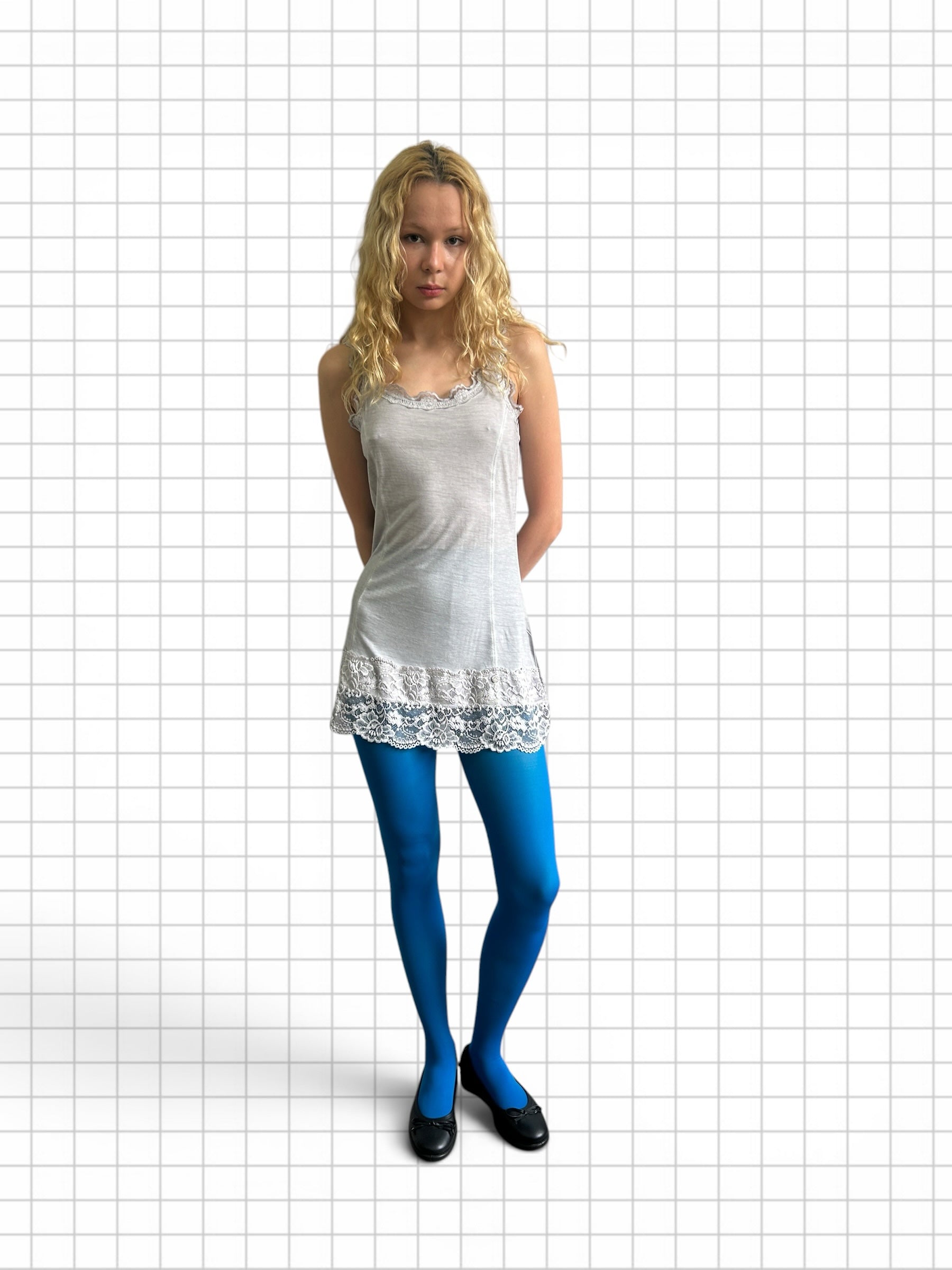 Wieder Wieder model wearing a white lace-trimmed camisole dress and vibrant blue tights against a grid background.