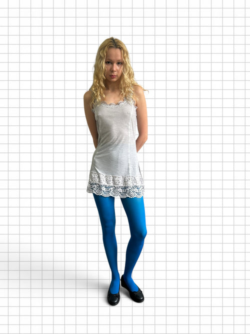 Wieder Wieder model wearing a white lace-trimmed camisole dress and vibrant blue tights against a grid background.